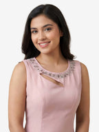 Woman wearing a pink dress with embellished neckline against a beige background