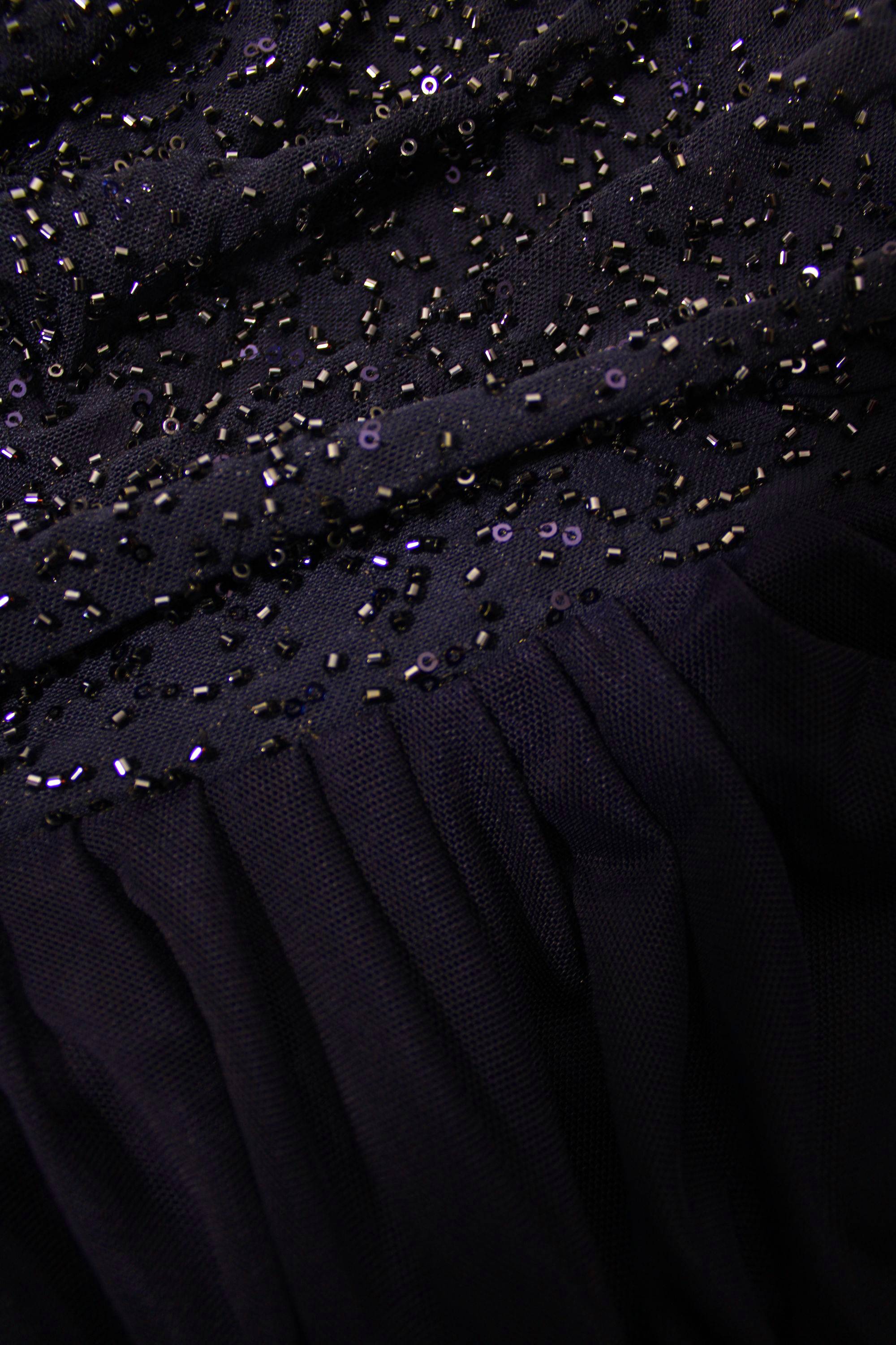 Close-up of a black dress with bead embellishments on a dark background
